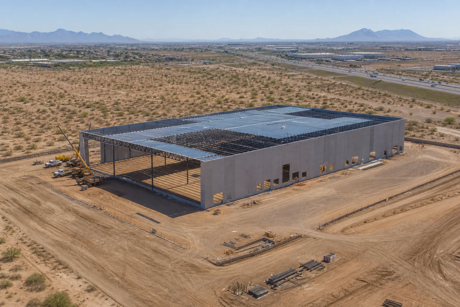 Aerial view of a new commercial building under construction on a graded lot in Peoria, Arizona, with the West Valley landscape in the background