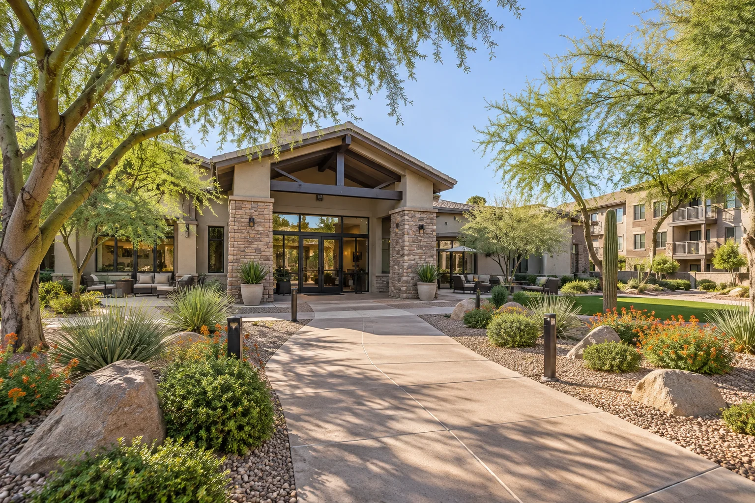 Manicured desert landscaping and shade trees framing the clubhouse entrance of a multifamily apartment complex
