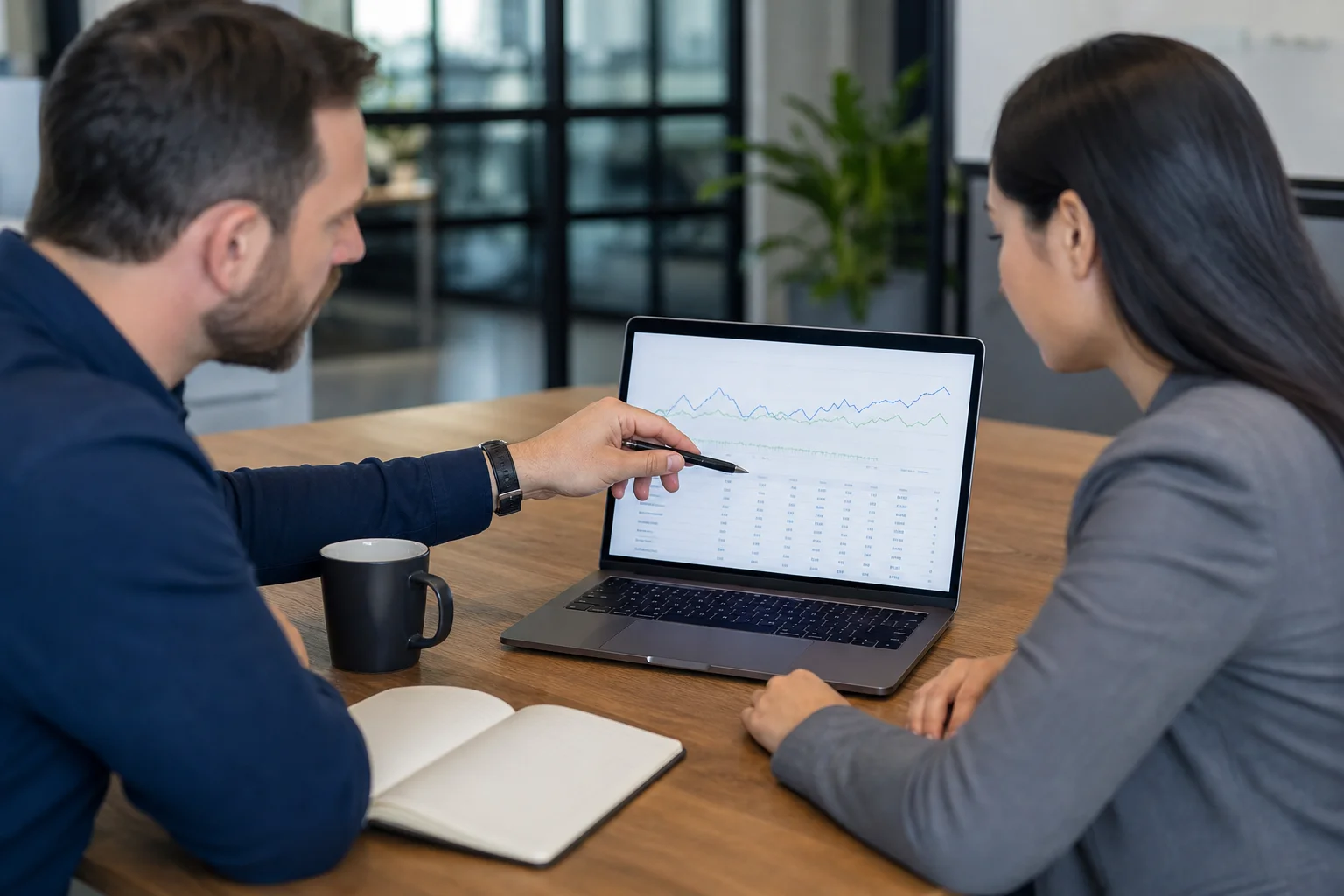 A marketing team reviewing SEO analytics and ranking charts on a laptop and monitor during an agency handoff meeting
